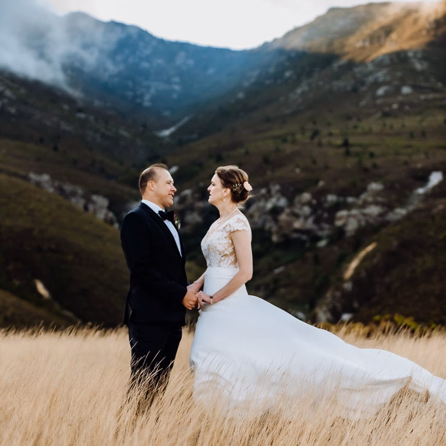 A newly married couple standing in a field below the mountain