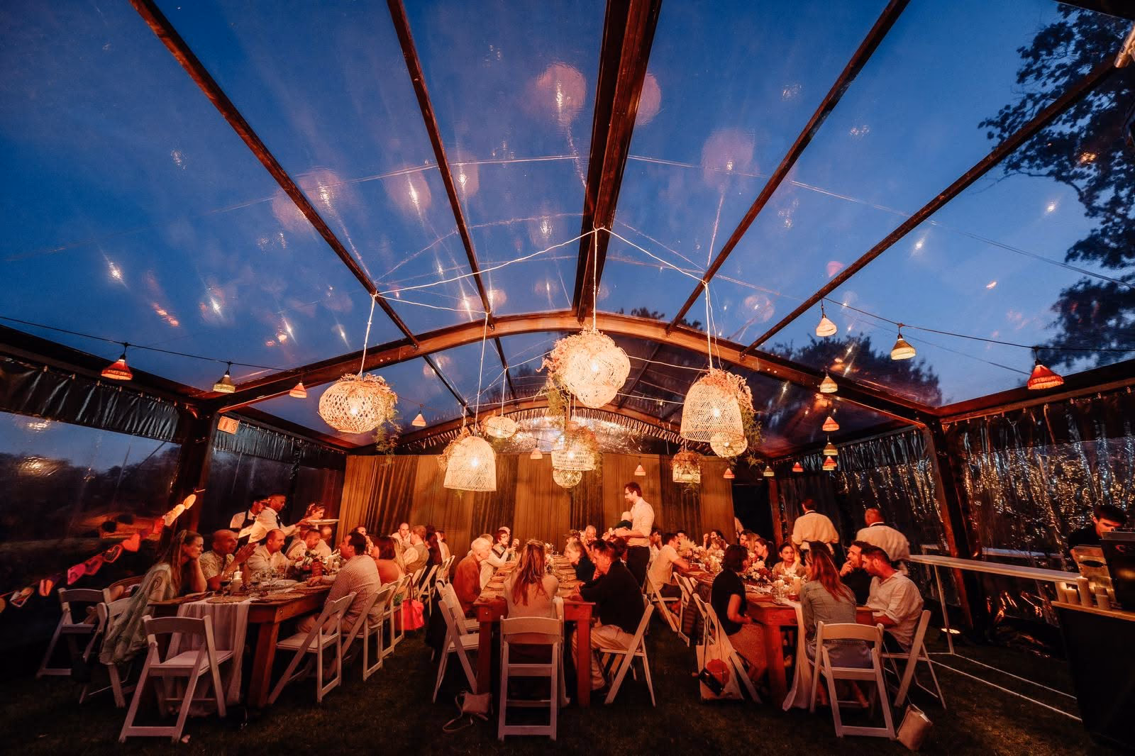 Guests dining beneath a clear roof at blue hour